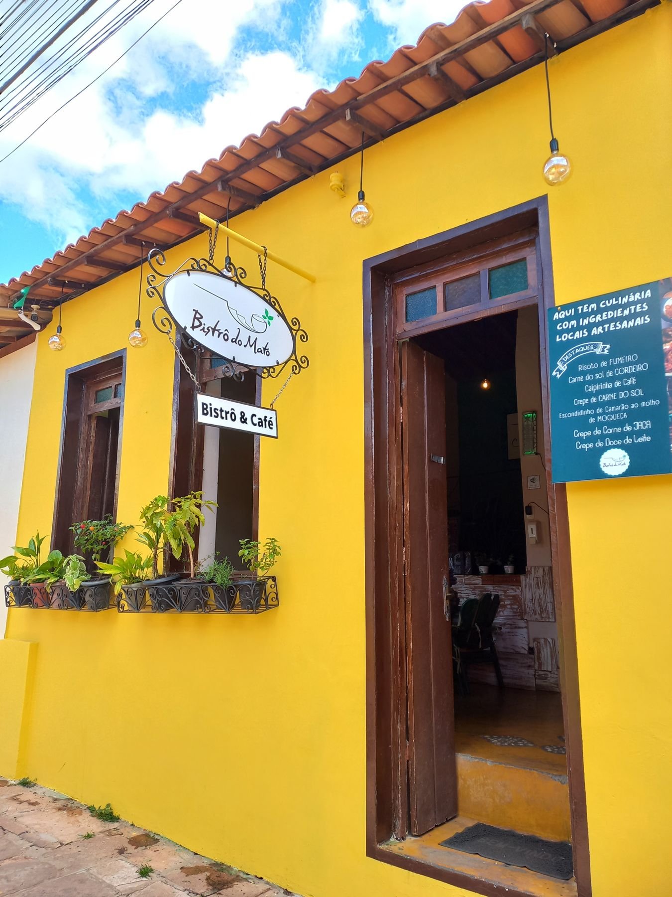 Casa amarela do Bistrô do Mato com as portas abertas para a rua de pedras