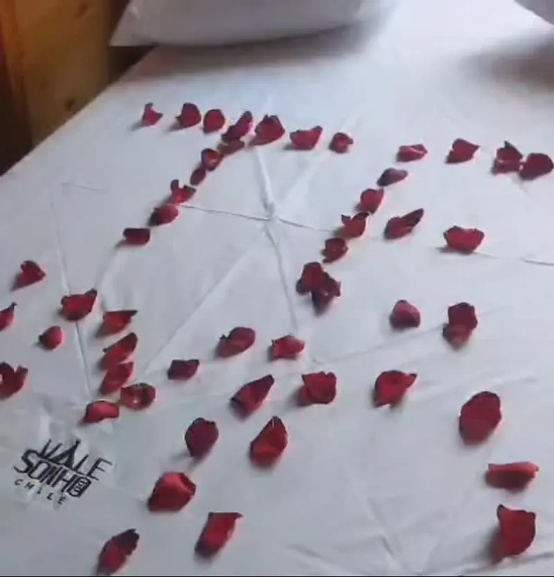Cama de casal com pétalas de rosa e o logo do chalé bordado no lençol