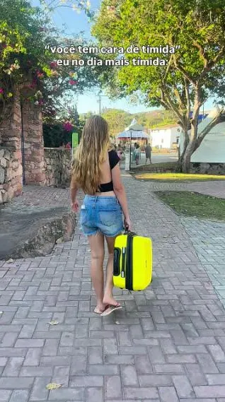 Clara caminhando com mala amarela em uma praça