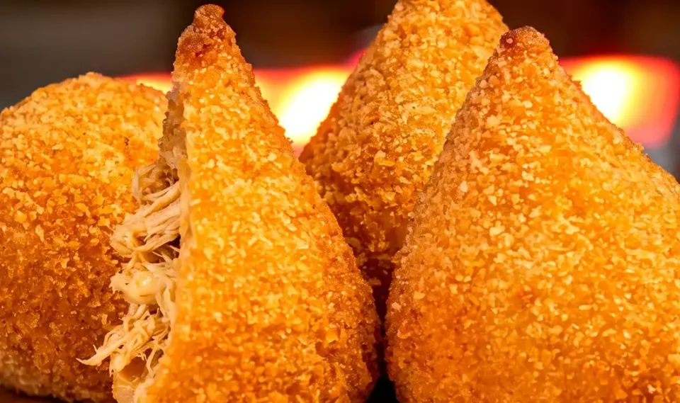 Coxinhas douradas, uma delas partida mostrando o recheio de frango desfiado